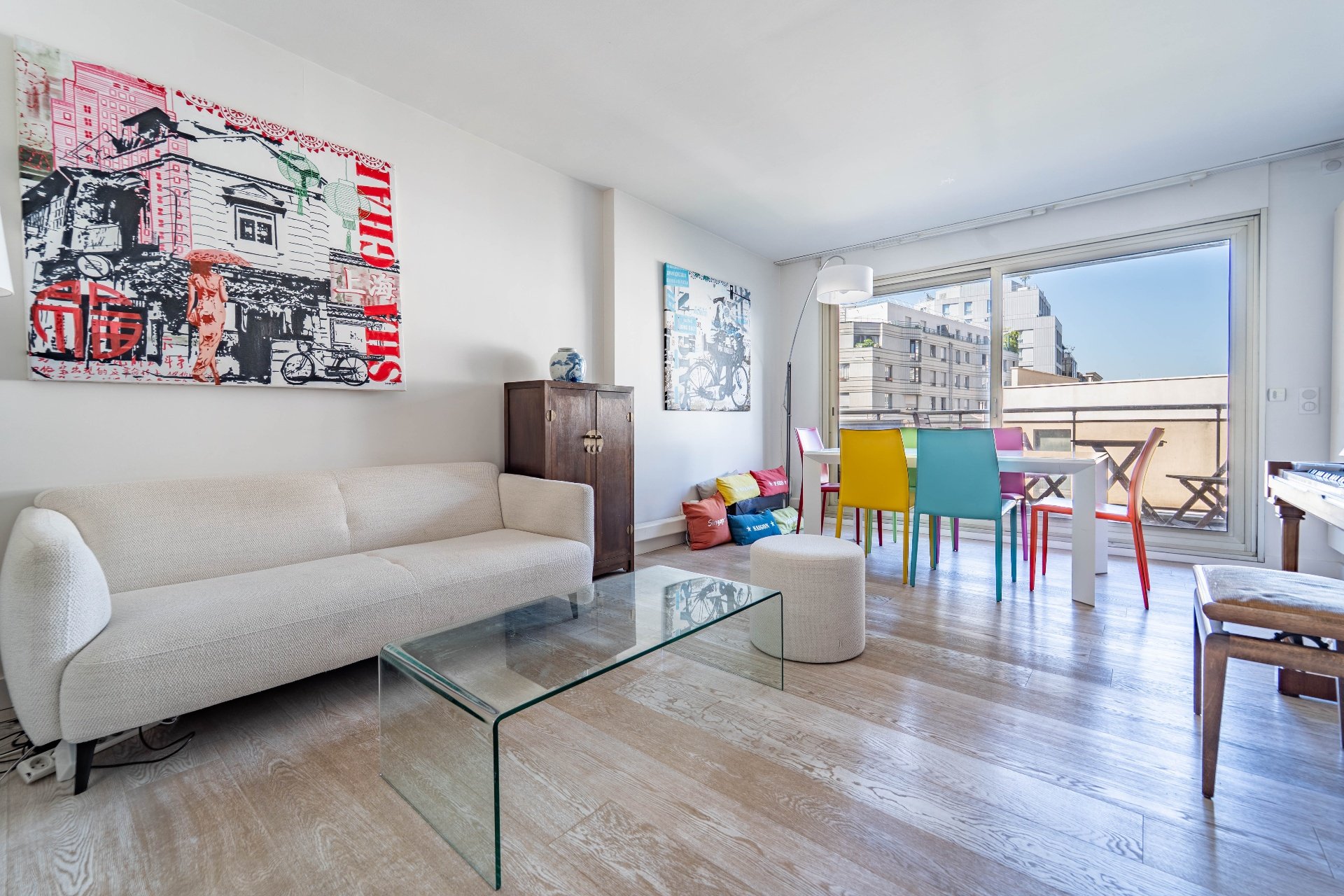 Séjour lumineux avec canapé beige, table basse en verre et chaises colorées