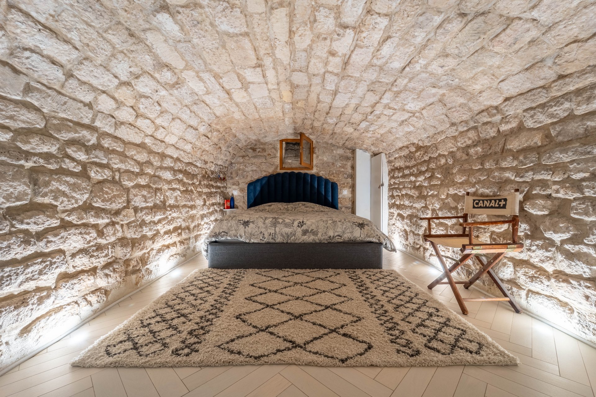 Chambre voûtée en pierres apparentes avec tête de lit velours bleu et tapis berbère