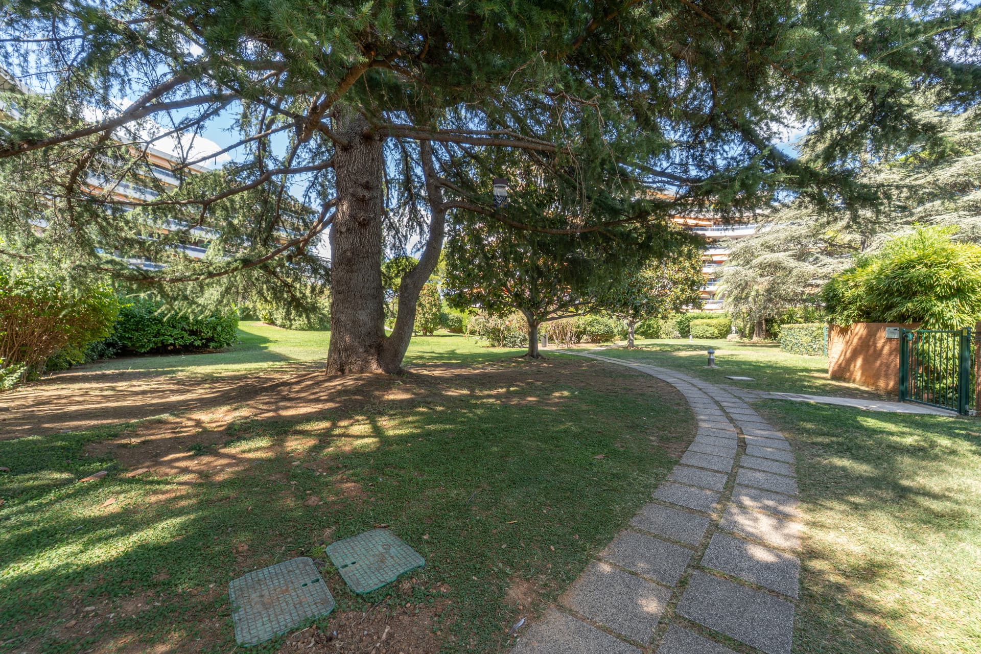 Parc arboré de la résidence avec pelouse et chemin pavé
